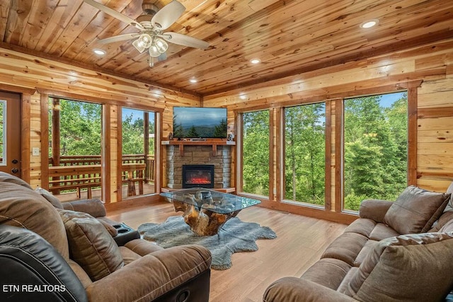 living room featuring wooden ceiling, a stone fireplace, a ceiling fan, healthy amount of natural light, and wooden walls