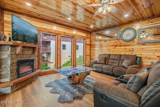 living room featuring wood ceiling, a ceiling fan, wood finished floors, wooden walls, and a stone fireplace