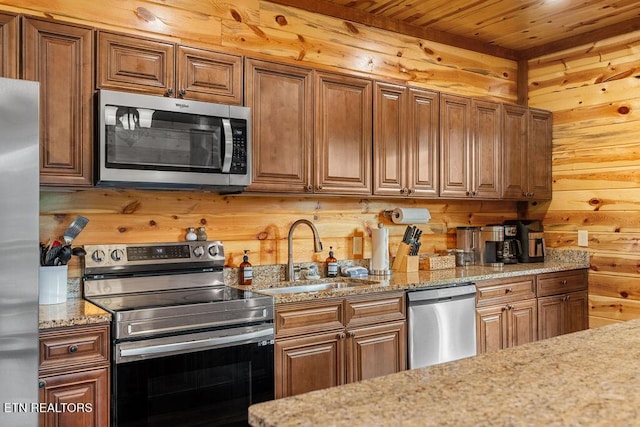 kitchen with appliances with stainless steel finishes, a sink, wood walls, light stone counters, and wood ceiling