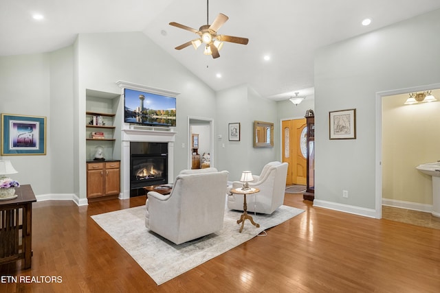 living area featuring ceiling fan, a glass covered fireplace, high vaulted ceiling, dark wood finished floors, and baseboards