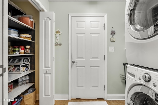 clothes washing area featuring stacked washer and clothes dryer, baseboards, and tile patterned flooring
