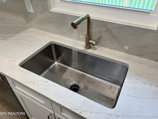 kitchen view of a sink, light stone counters, and white cabinetry