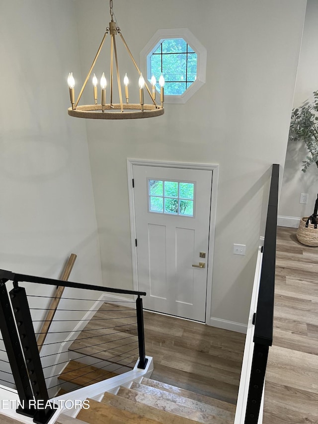 foyer entrance with a chandelier, wood finished floors, healthy amount of natural light, baseboards, and a towering ceiling