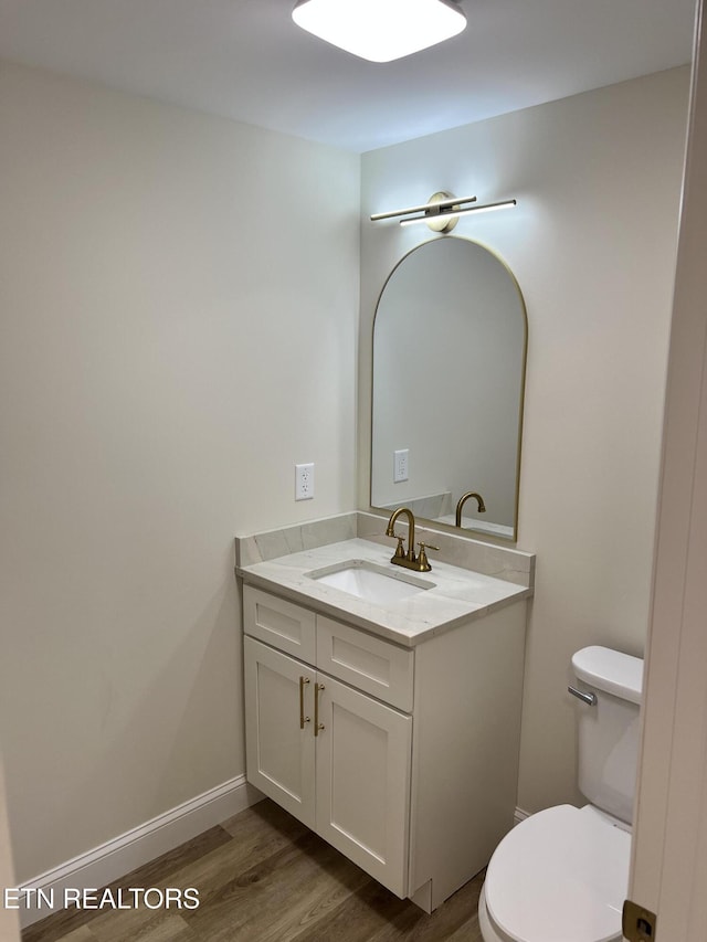 half bath featuring wood finished floors, vanity, toilet, and baseboards