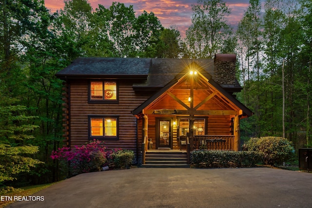 log-style house featuring covered porch, log siding, and a chimney