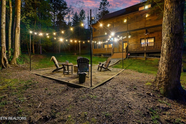yard at dusk featuring a deck, a lawn, an outdoor fire pit, and a patio area