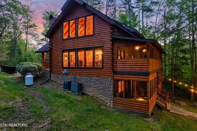 rear view of property with a chimney, log siding, a yard, and central AC