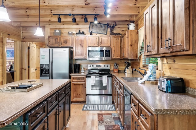 kitchen featuring appliances with stainless steel finishes, track lighting, light wood-style floors, a sink, and decorative light fixtures