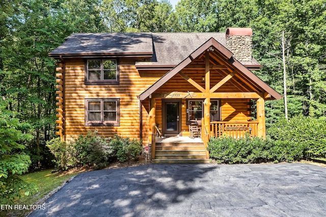 log home with a chimney, covered porch, a shingled roof, and log exterior