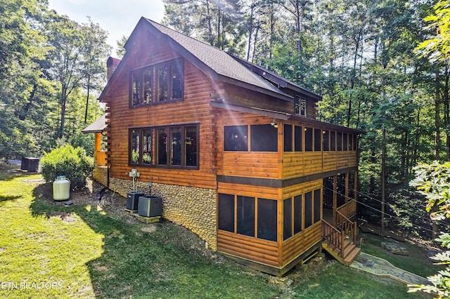 view of home's exterior featuring a sunroom, a chimney, a lawn, and log exterior