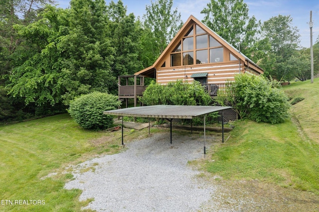 back of property featuring gravel driveway, a detached carport, a wooden deck, and a lawn
