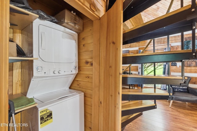 washroom with stacked washer and clothes dryer, hardwood / wood-style flooring, and wooden walls