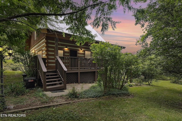 back of property at dusk featuring log siding, a lawn, and a deck