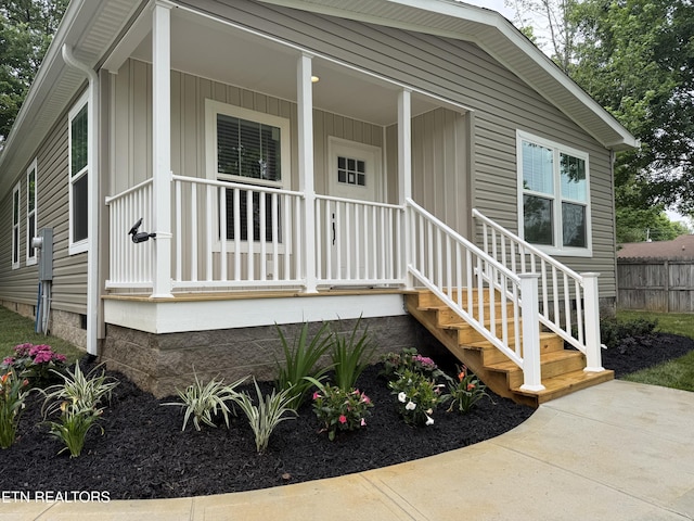 doorway to property featuring a porch, board and batten siding, and fence