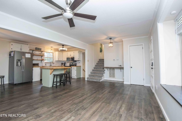 living area featuring dark wood-type flooring, ceiling fan, crown molding, baseboards, and stairs