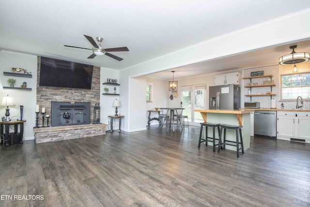 living room featuring a ceiling fan, a fireplace, dark wood-style flooring, crown molding, and baseboards
