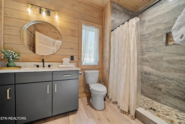 full bathroom with toilet, wood finished floors, wood walls, vanity, and tiled shower