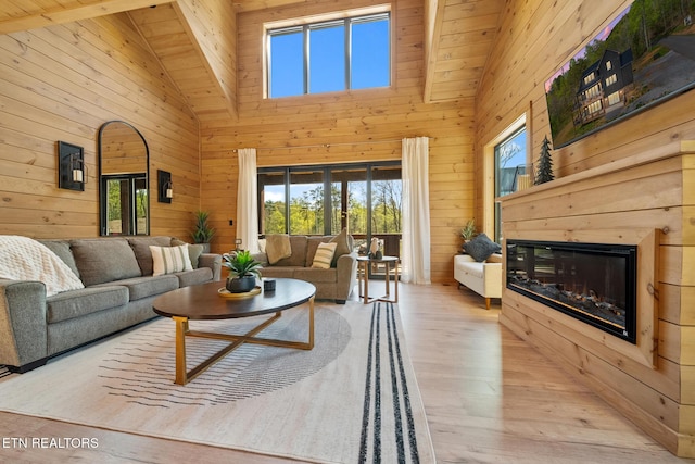 living room with plenty of natural light, wood walls, a glass covered fireplace, hardwood / wood-style floors, and high vaulted ceiling