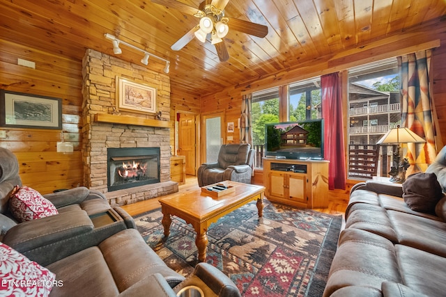 living area with a ceiling fan, wood finished floors, wooden walls, a stone fireplace, and wood ceiling