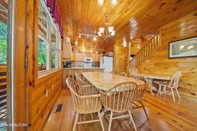 dining space featuring light wood-style floors, a chandelier, wooden walls, and wooden ceiling