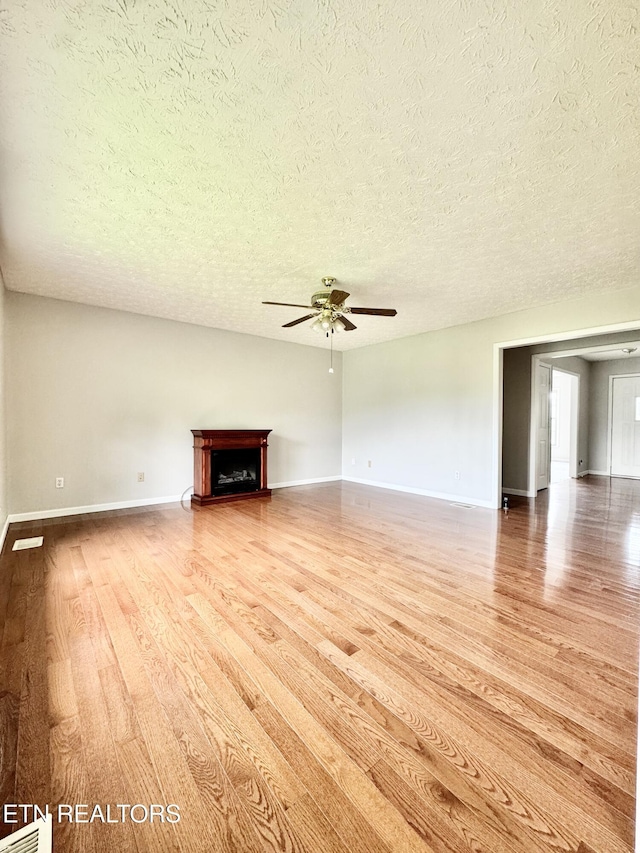 200 Harmon Cir, New Tazewell, TN 37825 - unfurnished living room featuring ceiling fan, a textured ceiling, wood finished floors, baseboards, and a fireplace with raised hearth