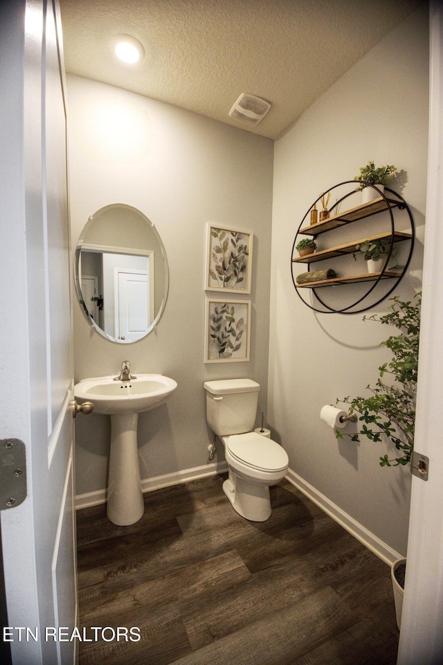 half bath with wood finished floors, toilet, baseboards, a textured ceiling, and a sink