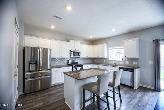 kitchen with appliances with stainless steel finishes, a kitchen island, backsplash, white cabinetry, and a textured ceiling