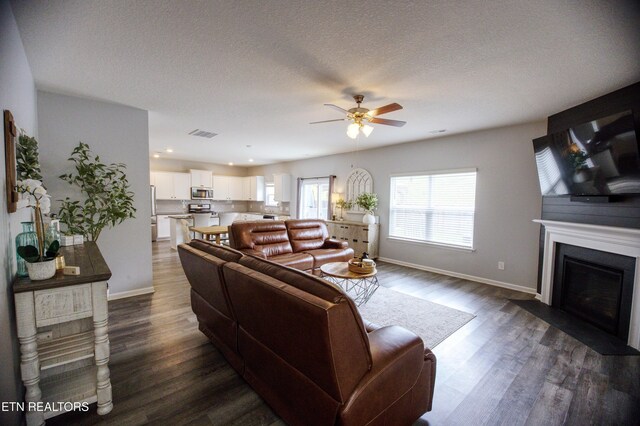living room featuring ceiling fan, dark wood finished floors, baseboards, a fireplace with flush hearth, and a textured ceiling