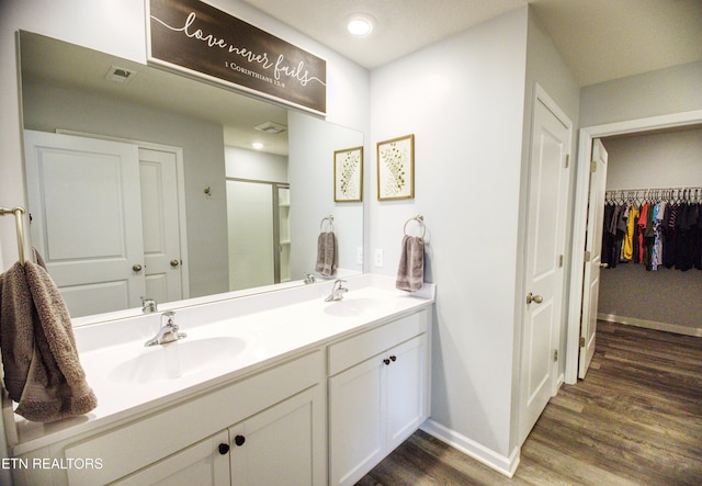 full bath featuring wood finished floors, a stall shower, double vanity, baseboards, and a spacious closet