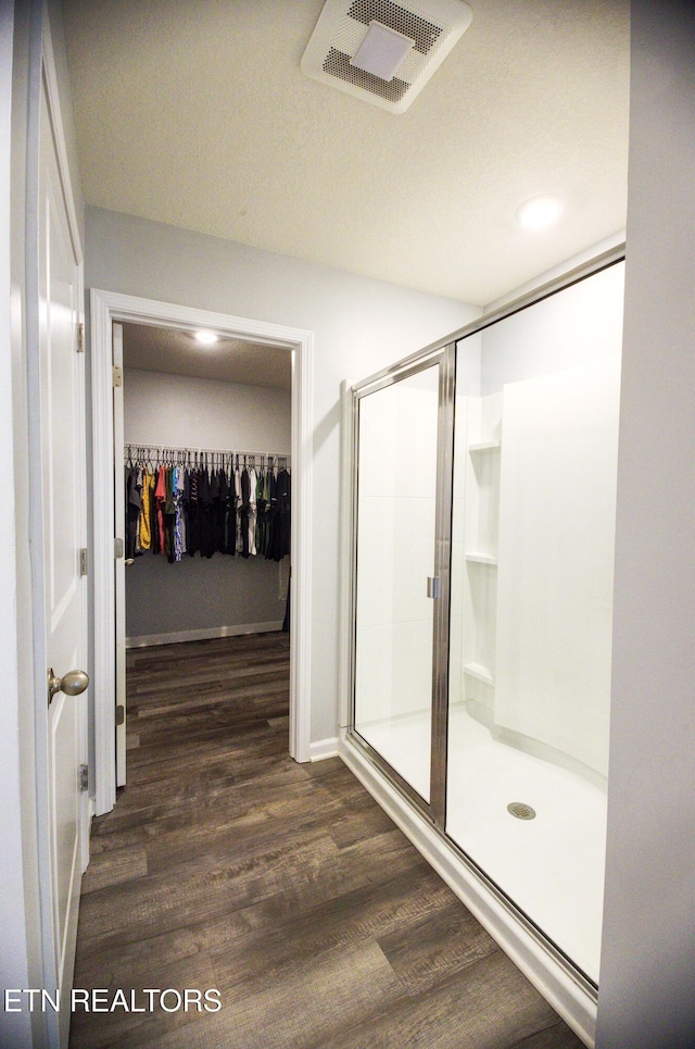 bathroom with wood finished floors, a shower stall, and a walk in closet