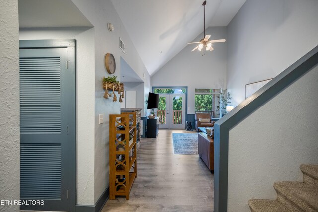 living area with wood finished floors, stairway, french doors, a ceiling fan, and high vaulted ceiling