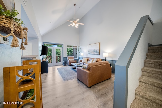 living room featuring high vaulted ceiling, light wood-type flooring, stairs, french doors, and ceiling fan