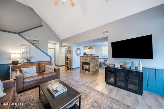living area with wood finished floors, a ceiling fan, a fireplace, and high vaulted ceiling