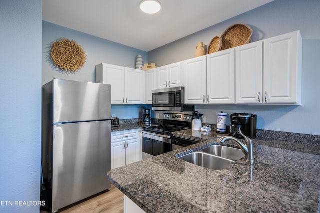 kitchen with appliances with stainless steel finishes, a sink, white cabinets, dark stone counters, and light wood-type flooring