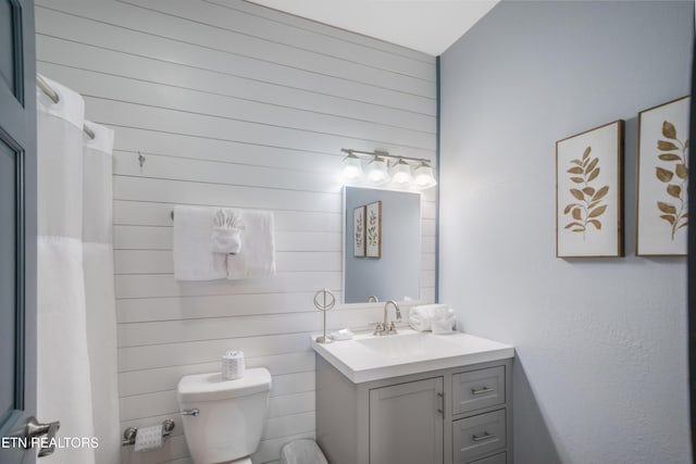 bathroom with wood walls, vanity, and toilet
