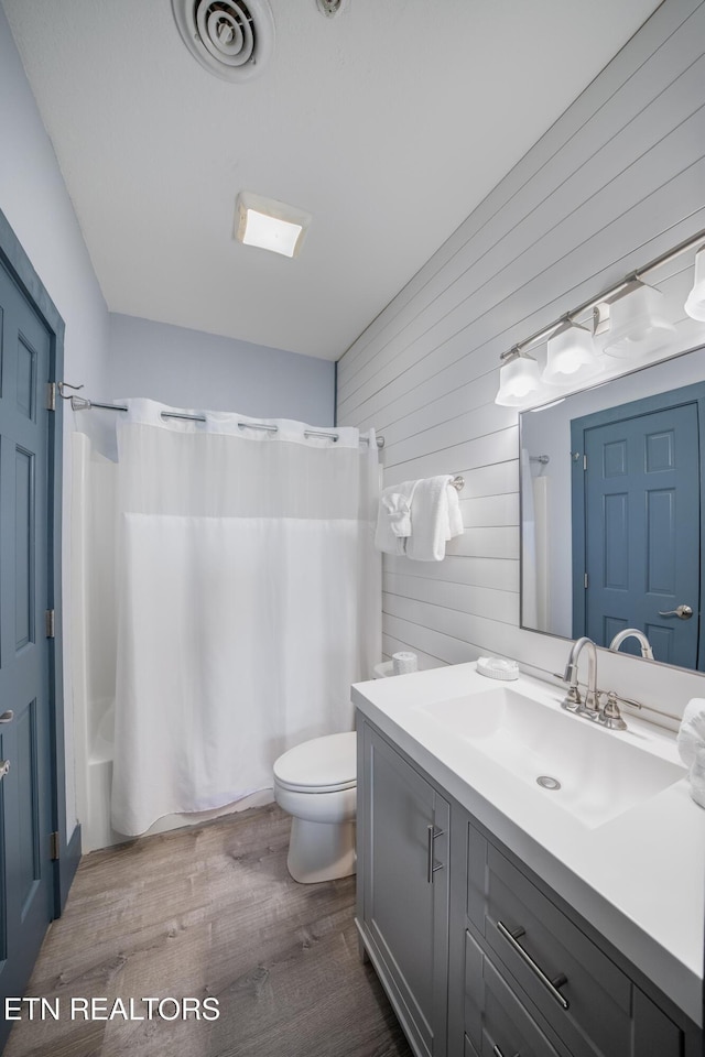 full bath with wooden walls, toilet, wood finished floors, shower / bathtub combination with curtain, and vanity
