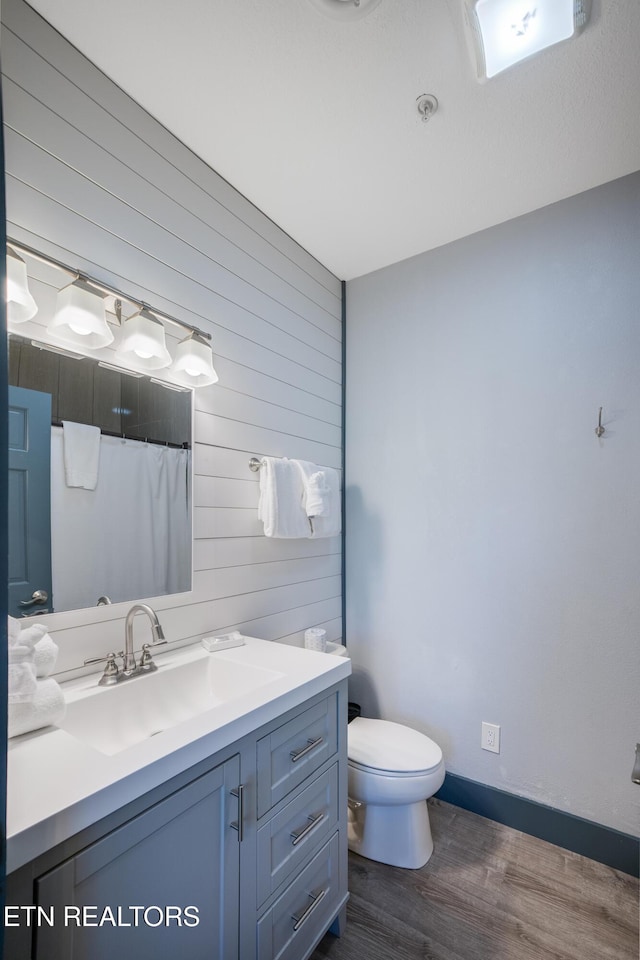 bathroom featuring wooden walls, wood finished floors, vanity, toilet, and baseboards