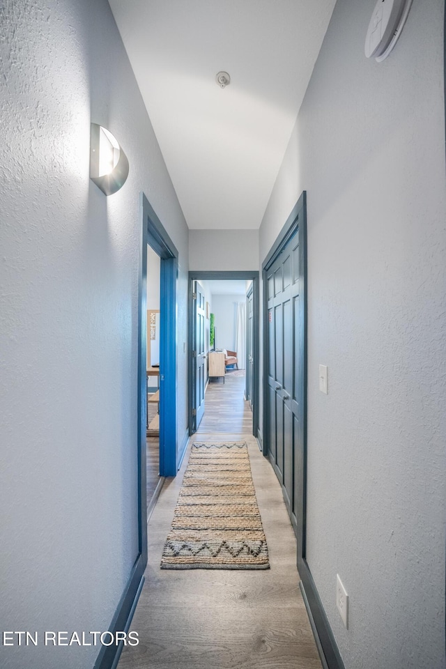 corridor with baseboards, light wood-style flooring, and a textured wall