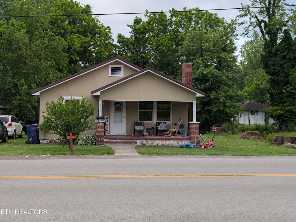 515 Winchester Ave, Middlesboro, KY 40965 - bungalow with covered porch, stucco siding, a front lawn, a chimney, and view of wooded area