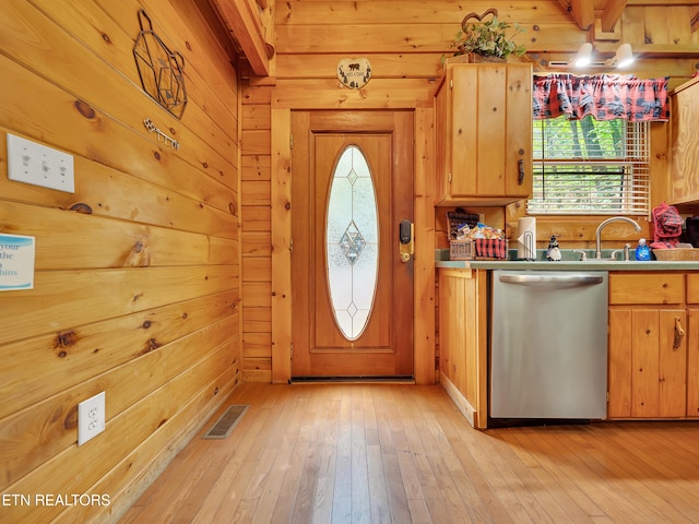 kitchen with stainless steel dishwasher, plenty of natural light, light wood-style floors, wood walls, and a sink
