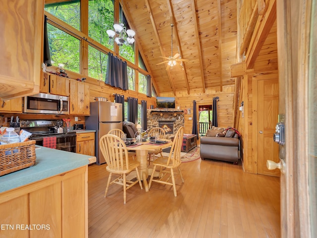 dining room featuring high vaulted ceiling, a stone fireplace, wooden walls, light wood-style floors, and wooden ceiling with exposed beams