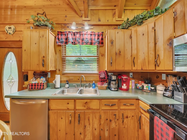 kitchen featuring appliances with stainless steel finishes, a sink, light countertops, and wood walls