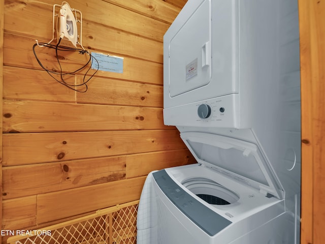 washroom with stacked washing machine and dryer and wooden walls