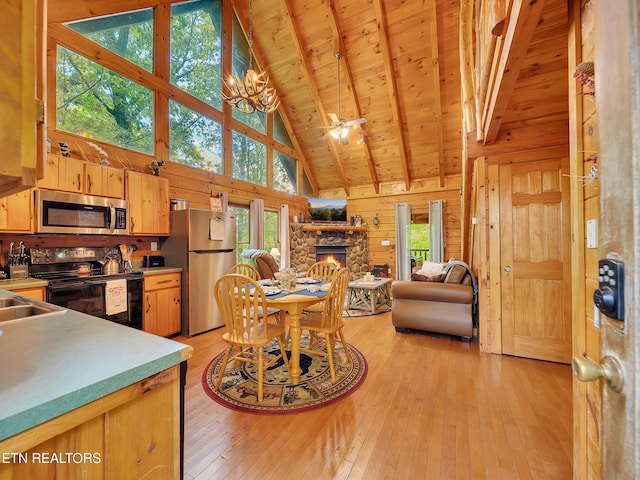 dining room with high vaulted ceiling, a stone fireplace, light wood-style flooring, wooden ceiling with exposed beams, and wooden walls