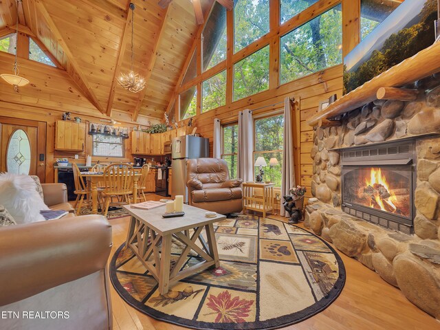 living area featuring high vaulted ceiling, light wood-style flooring, plenty of natural light, wooden walls, and a stone fireplace