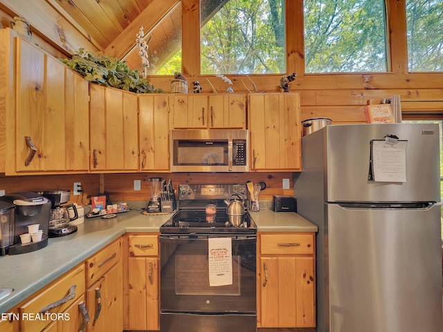 kitchen with stainless steel appliances, plenty of natural light, light countertops, lofted ceiling, and wooden walls