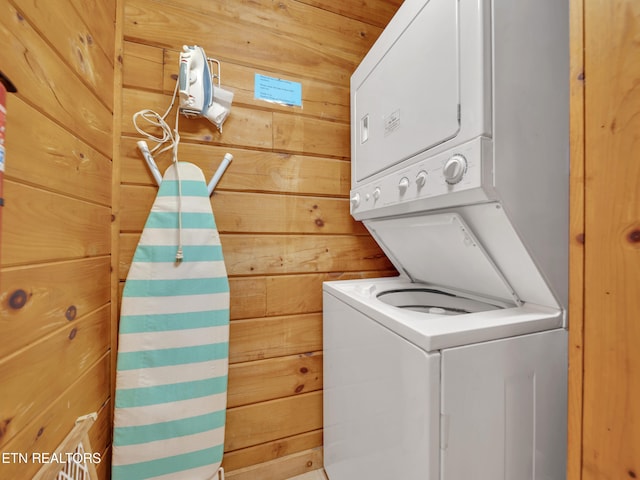 laundry area with stacked washer and clothes dryer and wood walls