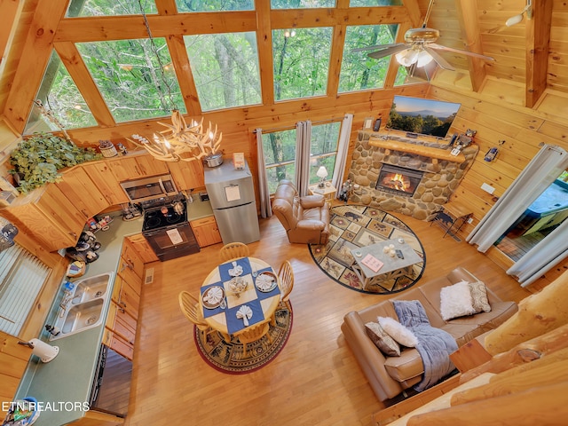 living room with a chandelier, wood finished floors, a towering ceiling, a stone fireplace, and wood walls