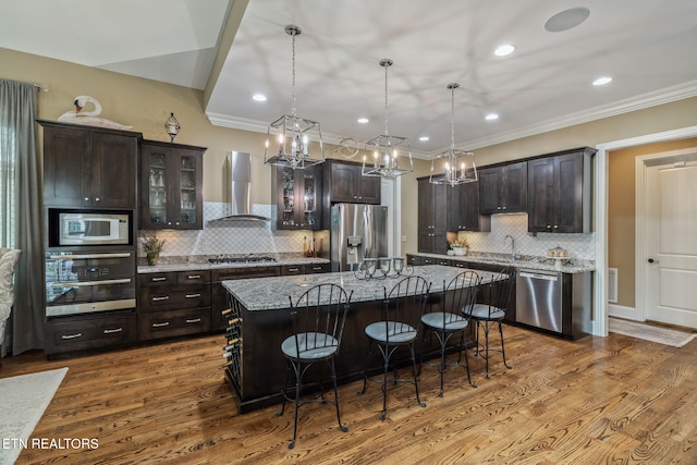 111 Winchester Cir, Oak Ridge, TN 37830 - kitchen with wall chimney range hood, appliances with stainless steel finishes, a breakfast bar, dark brown cabinetry, and recessed lighting
