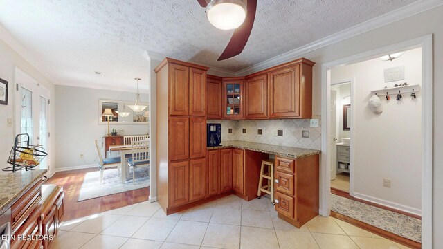 1859 Poplar Hill Rd, Knoxville, TN 37922 - kitchen with brown cabinetry, light stone countertops, light tile patterned floors, ornamental molding, and a textured ceiling